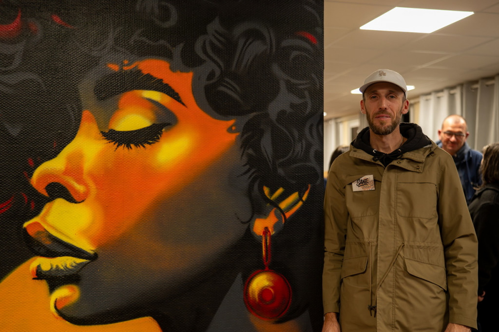 L'artiste Sane, qui a réalisé les peintures murales de la résidence avec l'artiste Otantic, pose à côté d'un visage qu'ils ont peint pour la résidence.